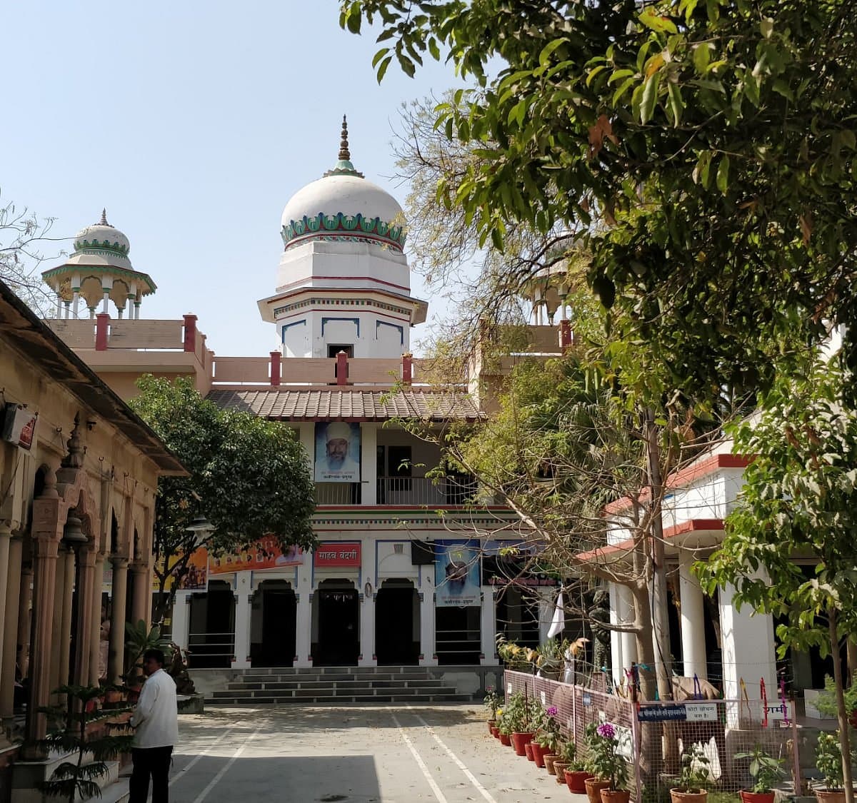 The inner compound of a spiritual center with white domes and traditional architecture, surrounded by potted plants and greenery